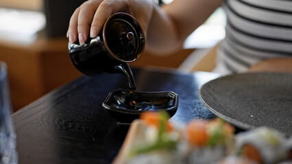 Young beautiful hispanic woman pouring soja sauce at the restaurant