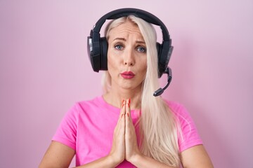 Caucasian woman listening to music using headphones begging and praying with hands together with hope expression on face very emotional and worried. begging.