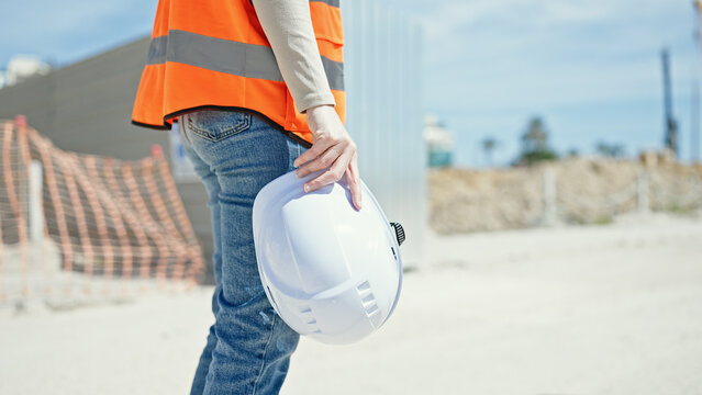 Young beautiful hispanic woman builder holding hardhat at street