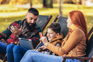 Young family enjoying time in a outdoor cafe using digital tablet for online shopping.