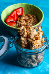 Healthy breakfast with granola and fresh strawberries served in a bowl on a blue background. Minimalistic composition with plate, spoon and natural morning light.