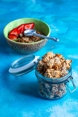 Healthy breakfast with granola and fresh strawberries served in a bowl on a blue background. Minimalistic composition with plate, spoon and natural morning light.