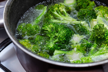 Boiling raw brocoli in water  in metal boiling pan. Green vegetables cooking .