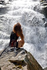 Femme assis sur une pierre devant une cascade chute d'eau puissante