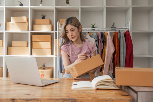 Woman designer stylish blogger entrepreneur is write the customer name in front of the box and taking receive online delivery order to prepare packing the product online shopping delivery