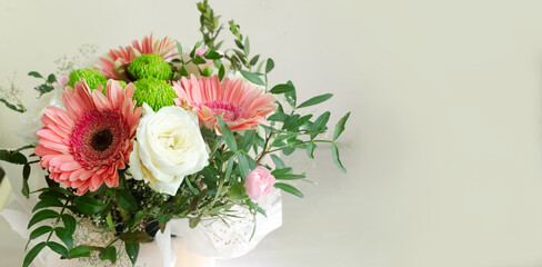Obraz na płótnie Canvas festive bouquet of white roses, pink gerberas and carnations in frame of green twigs on a light background. Birthday. Mother's Day. The concept of holiday flowers. Selective focus. Banner. Copy space