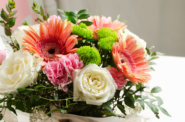 festive bouquet of white roses, pink gerberas and carnations in a frame of green twigs on a light background. Birthday. Mother's Day. The concept of holiday flowers. Selective focus.
