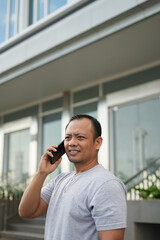Portrait of Asian man talking on phone while in front of office
