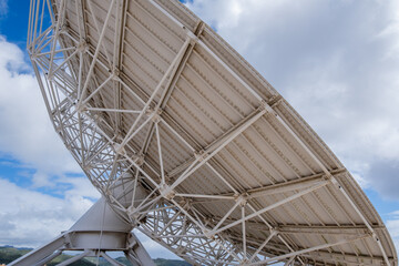 Detail of the metal beam structure of a large white satellite dish for stargazing, with large white clouds in the background. Museum of science and the cosmos. Tenerife, Canary Islands, Spain