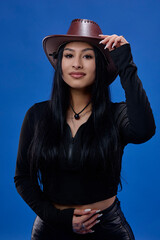 a young brunette with long hair and a hat posing in the studio isolated on a blue background.