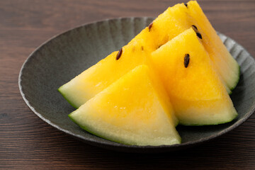 Sliced yellow watermelon in a plate on wooden table background.