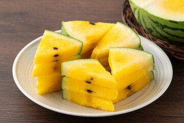 Sliced yellow watermelon in a plate on wooden table background.