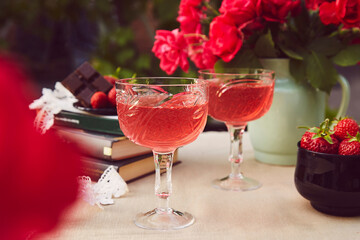 Aesthetics table setting. Couple of glasess with red homemade, strawberry infusion, wine. Roses bouquet. Summer background