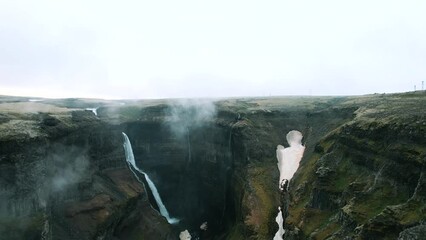 Drone shot revealing vast landscape of Haifoss waterfall surrounded by fog, Iceland - Powered by Adobe