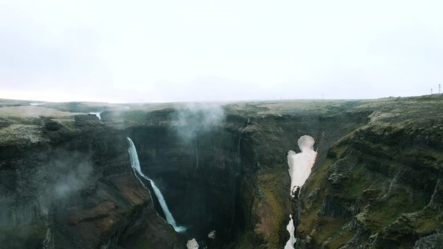 Drone shot revealing vast landscape of Haifoss waterfall surrounded by fog, Iceland