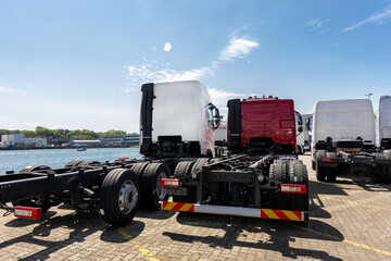 Back view many new heavy commercial cargo transport vehicles stand at port for export import shipping in Germany. Modern semi-trailer business industry truck tractor chassis sale sea logistics - obrazy, fototapety, plakaty