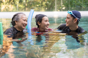 Young trainer helping senior woman in aqua aerobics and working out in the pool. old woman and mature man doing aqua aerobics exercise in swimming pool, Elderly sports, and active lifestyle concept.