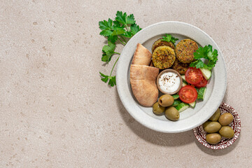 Falafel bowl with salad, yogurt sauce and pita bread. Modern bright vegan food background with shadows