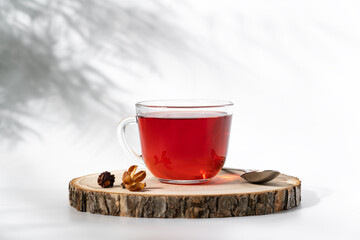 Hibiscus red tea in glass cup on wooden tray. Healthy natural drink close-up on white background with shadow