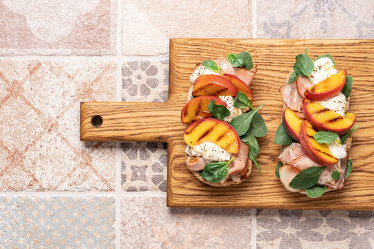 Peach prosciutto ham stracciatella cheese spinach bruschetta top view on portuguese ceramic tiles background. Delicious appetizer for wine