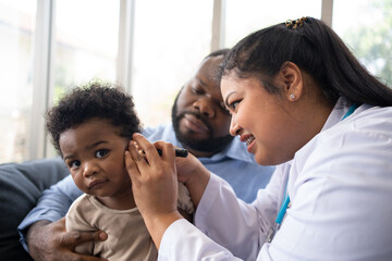 Pediatric doctor examining ear for a hearing test examining cute little girl in medical healthcare hospital or clinic. Smiling African American Baby whit pediatrician in hospital