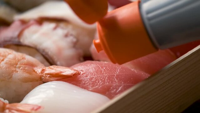 Adding soy sauce on tuna nigiri on a selection of varied Japanese sushi.