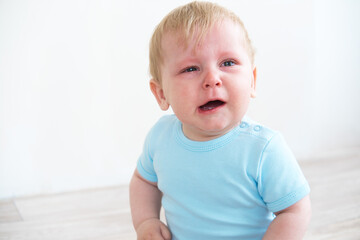 blonde baby in blue shirt crying sitting on floor at home