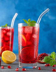 Iced red lemonade drink with fresh mint, sugar syrup and pomegranate juice in glass on a dark concrete background. Refreshing summer drink. Copy space.