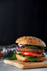 Veggie burger with with onion, cucumber and tomato on a black plate and black background