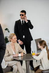 private security concept, successful happy mother and daughter spending time together in cafe, drinking coffee and orange juice, two bodyguards protecting safety of female clients