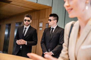 handsome bodyguards protecting successful client in hotel, woman on blurred foreground, security...