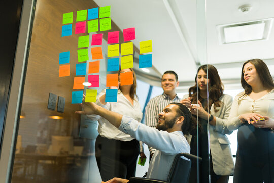 Disabled businessman pointing at sticky notes and brainstorming with co-workers