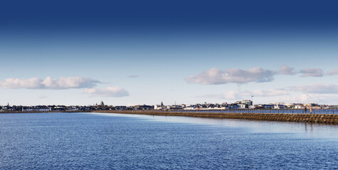 Fototapeta premium Panorama of Muttun island cause way with blue sky reflecting in the ocean surface. Galway city, Ireland, Irish landscape and architecture. Popular town landmark with view on Salthill promenade