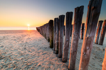 sunset on sand sea beach with wooden poles
