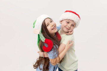 Merry Christmas and Happy New Year! A group of cheerful happy children in festive santa claus and elf hats on a white studio background. Children hug and have fun