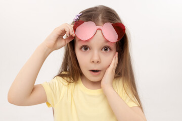 Portrait of surprised cute little toddler girl in the heart shape sunglasses. Child with open mouth having fun isolated over white background. Looking at camera. Wow funny face