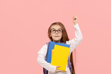 Portrait of a schoolgirl with textbooks and a backpack on a pink background points up. Back to school