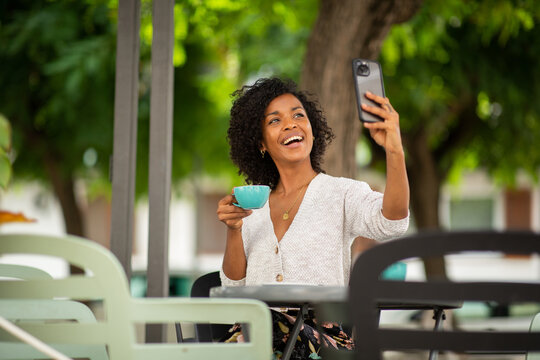 haopy african american woman holding cup of coffee and taking selfie with mobile phone