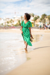 Full body smiling young woman walking by water on beach