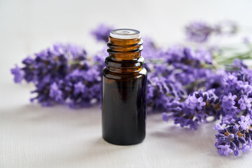 Essential oil bottle with lavender blossoms on bright background