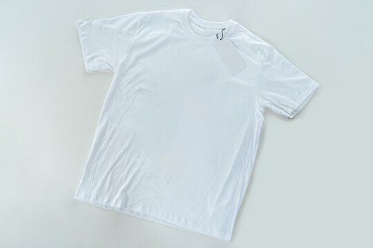 White t-shirt laying on the table, top view, full body with a blank sign of the logo hanging.