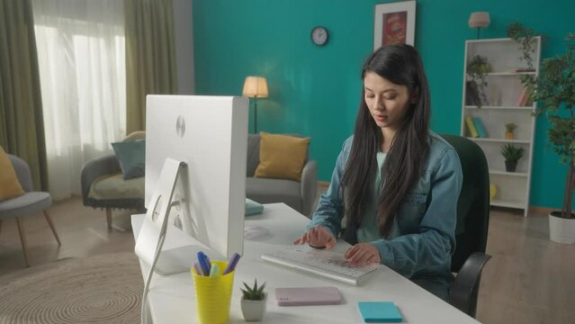 A Asian woman is talking on a smartphone while sitting at a computer. Woman ends conversation and gets to work, typing on keyboard, writing messages, chatting, freelancer. HDR BT2020 HLG Material.