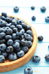 Fresh blueberry in wooden bowl on blue wooden background. Top view. Concept of healthy and dieting eating. Vertical photo