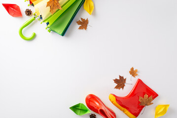 Enchanting autumn rain adventure for kids. Top-down photo featuring a colorful umbrella and rubber boots with maple leaves and paper boat on white isolated background, perfect for text or advertising