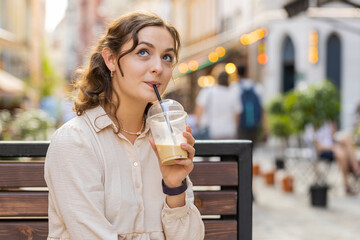Happy young woman enjoying morning cold coffee drink with ice and smiling outdoors. Relaxing,...