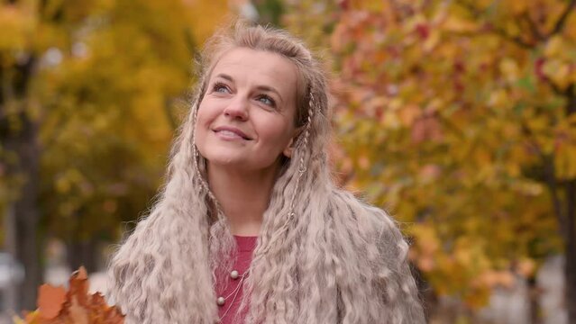 Portrait of a fashionable mature blonde woman with pigtails in a trendy beige coat in a city park in autumn. Happy middle aged woman enjoying autumn in the city
