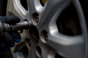 Close-up of a car mechanic removing caps from a black car with a drill at  a tire repair shop on the street detailing car repair
