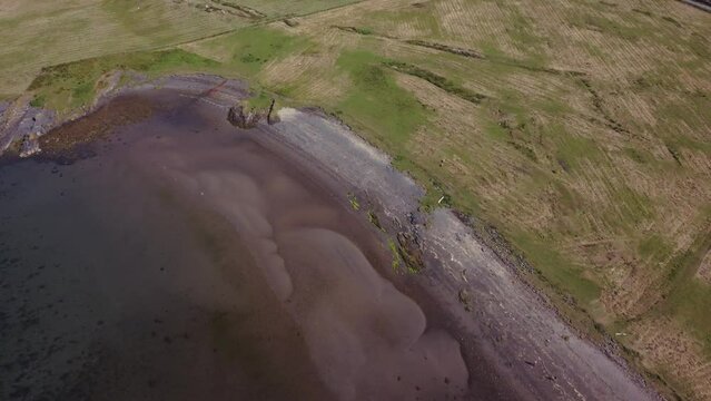 A swooping drone shot panning up from a deserted Scottish Island beach to reveal the wider landscape and distant islands in the background. Filmed on the remote Scottish Island of Luing in peak Summer