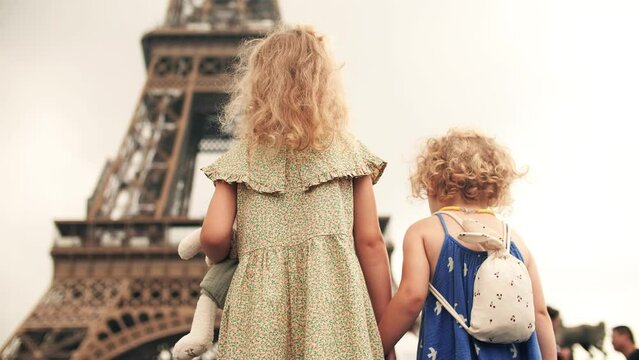 Two little sisters hold hands and look at the Eiffel Tower in Paris, France