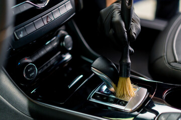 Car wash worker thoroughly cleaning the interior of a luxury car with a brush, gear box, close-up...